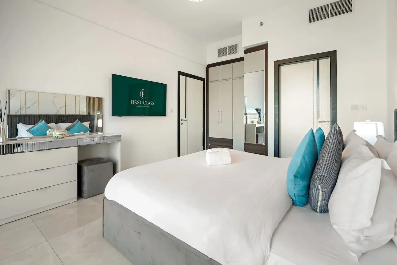 Un dormitorio luminoso con una cama tendida y cojines decorativos turquesa.