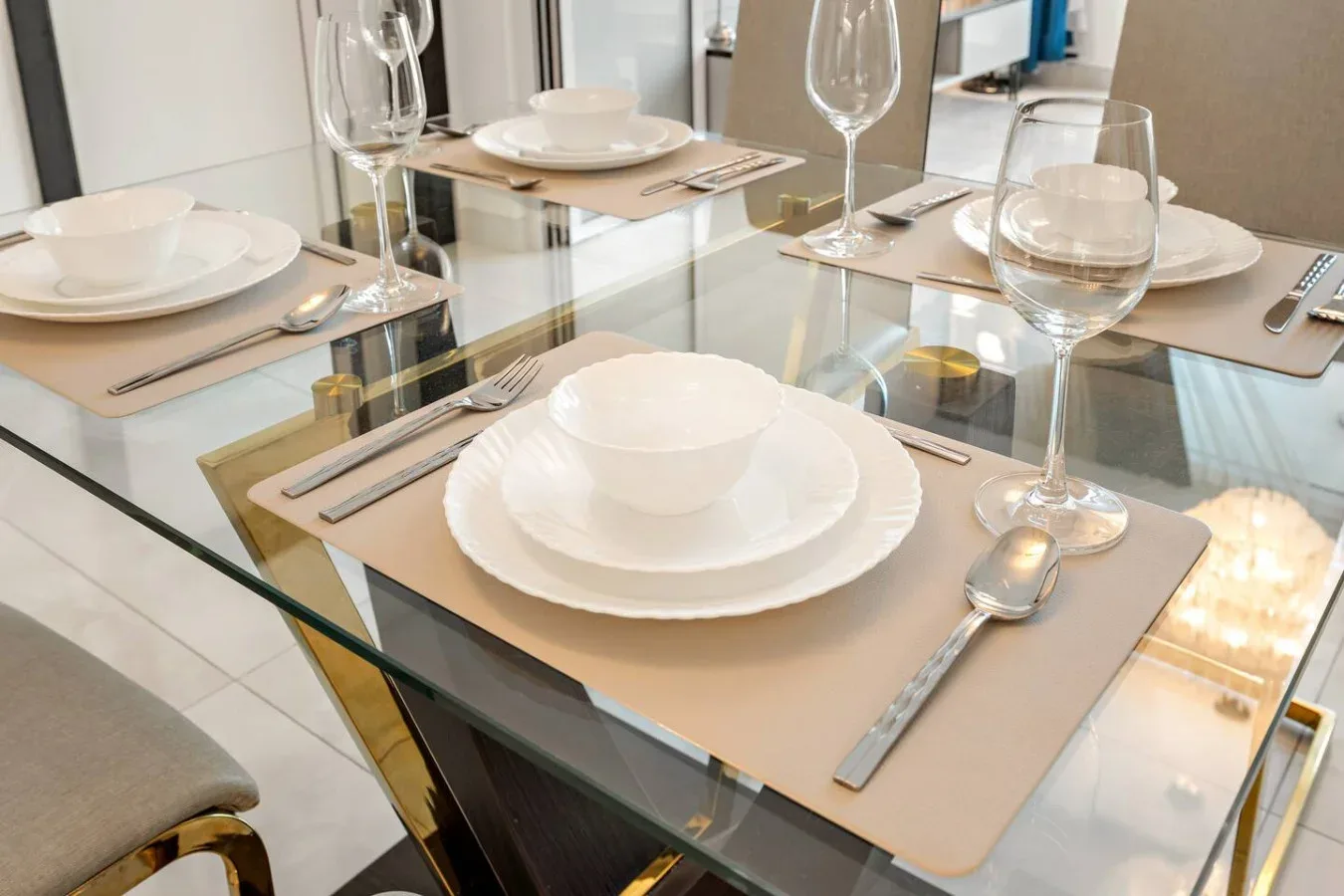Una mesa de comedor está preparada con platos blancos, manteles individuales y cristalería.