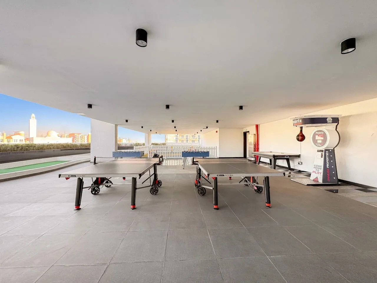 Una zona recreativa cubierta con mesas de ping-pong y una mesa de futbolín.