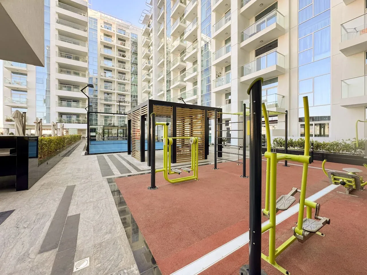 Una zona de ejercicio al aire libre con equipos se encuentra entre edificios de apartamentos modernos.