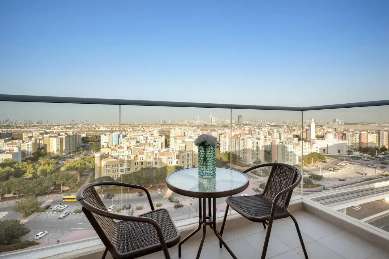 Una zona de estar en un balcón ofrece vistas de la ciudad a través de barandillas de vidrio.