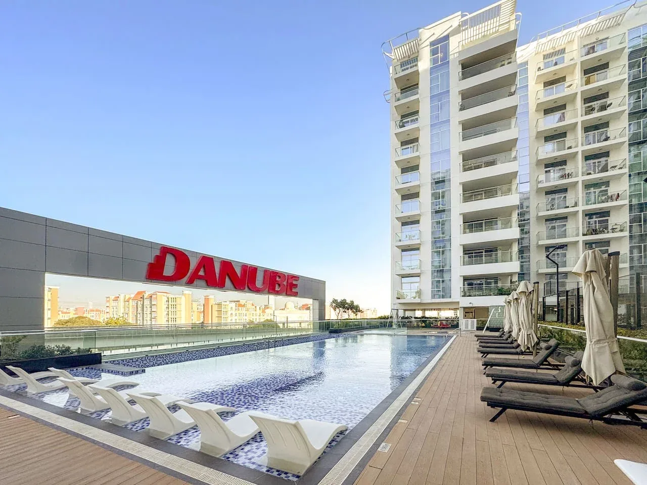 Una piscina al aire libre junto a un edificio alto, con tumbonas alrededor.