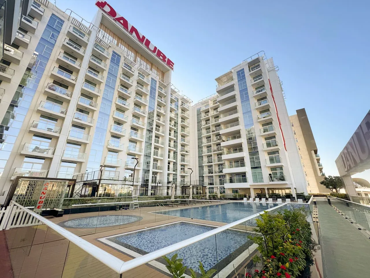 Un complejo de apartamentos moderno rodea un patio ajardinado con piscina.