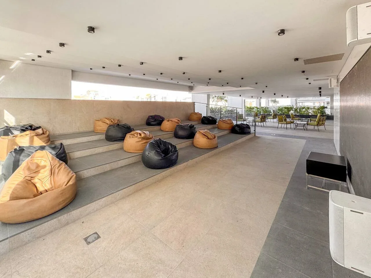 Una amplia sala tiene asientos escalonados, pufs y mesas junto a las ventanas.