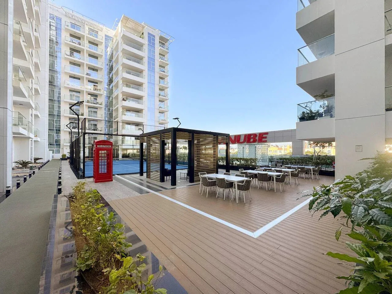 Zona exterior con mesas y un pabellón sombreado entre edificios de apartamentos modernos.