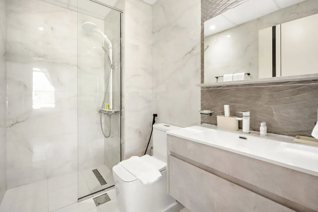 Un baño luminoso con ducha de cristal y un amplio tocador.