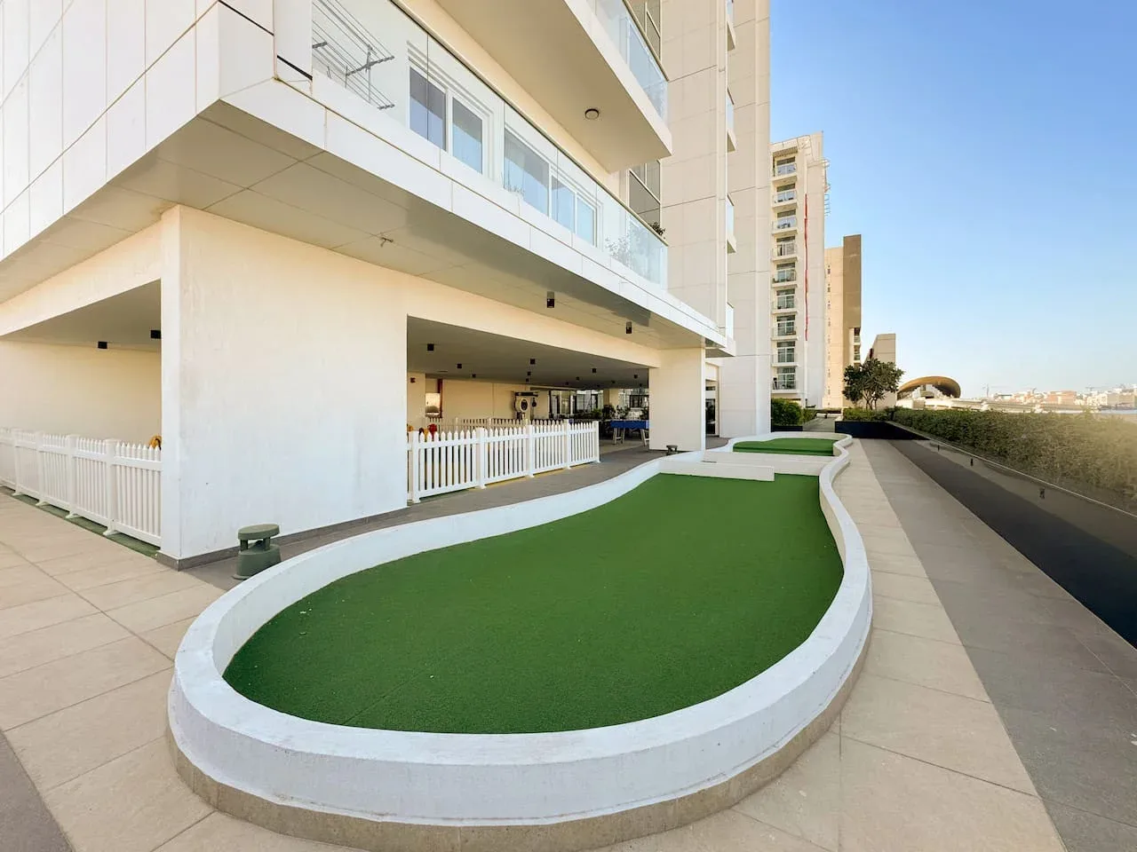 Una zona verde curva está junto a un edificio moderno y un camino pavimentado.