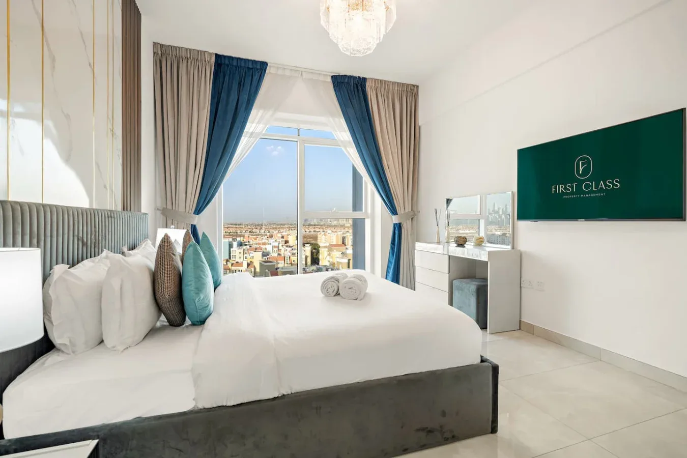 Un dormitorio con ropa de cama blanca, cortinas azules y una gran ventana con vistas a la ciudad.