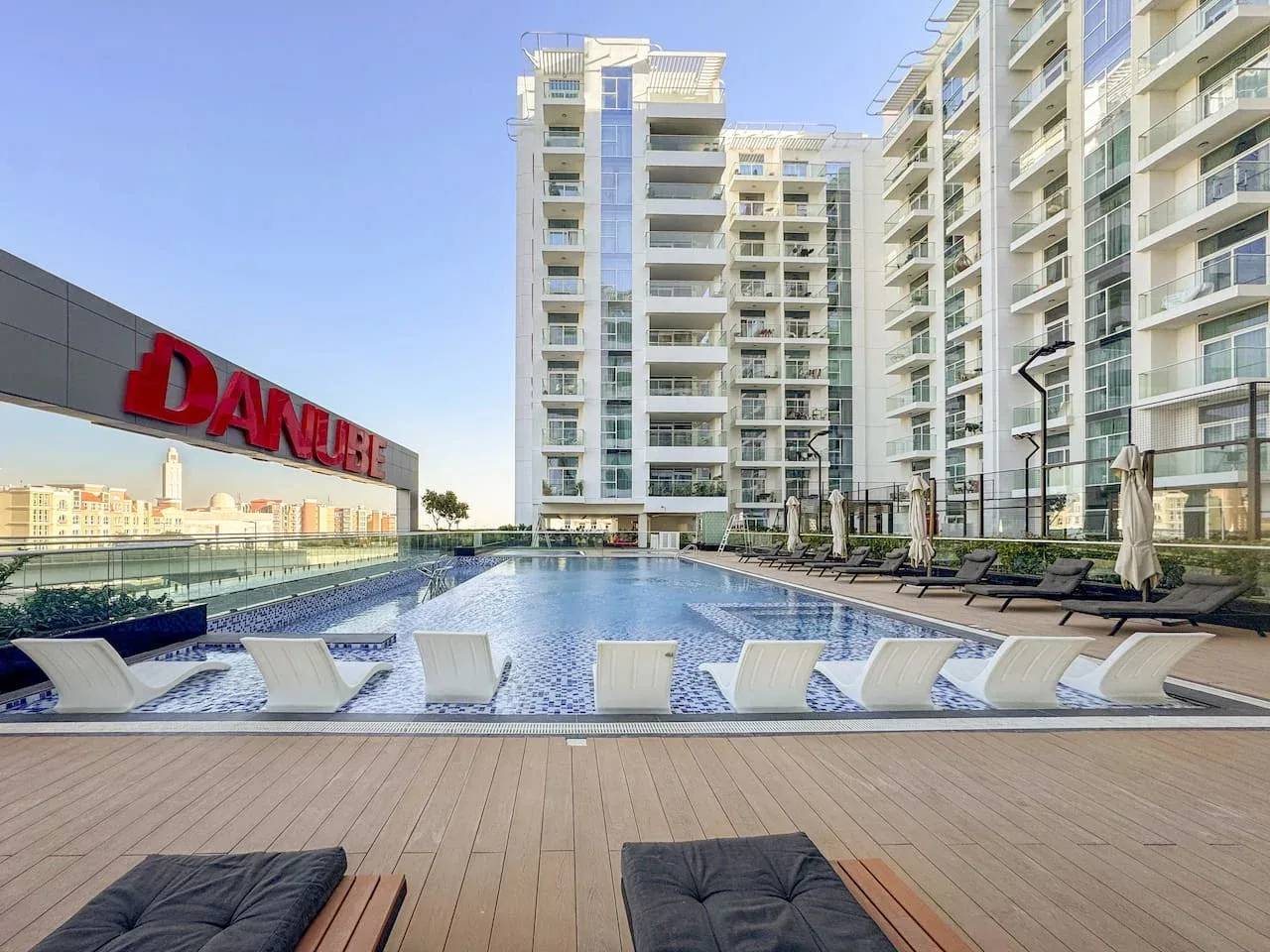Una piscina está junto a una terraza de madera y edificios de apartamentos modernos.