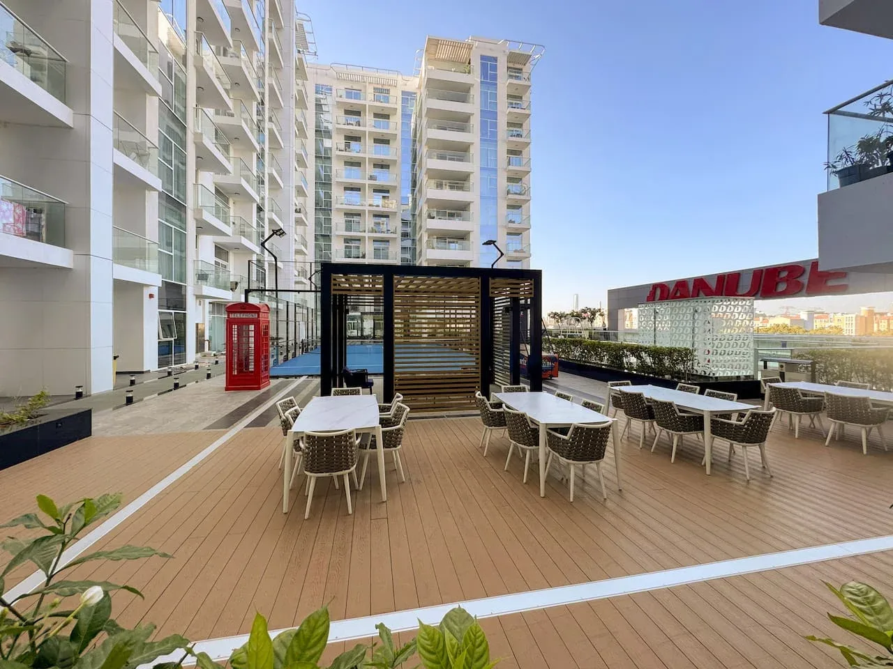 Una terraza exterior tiene mesas y asientos junto a un edificio moderno.