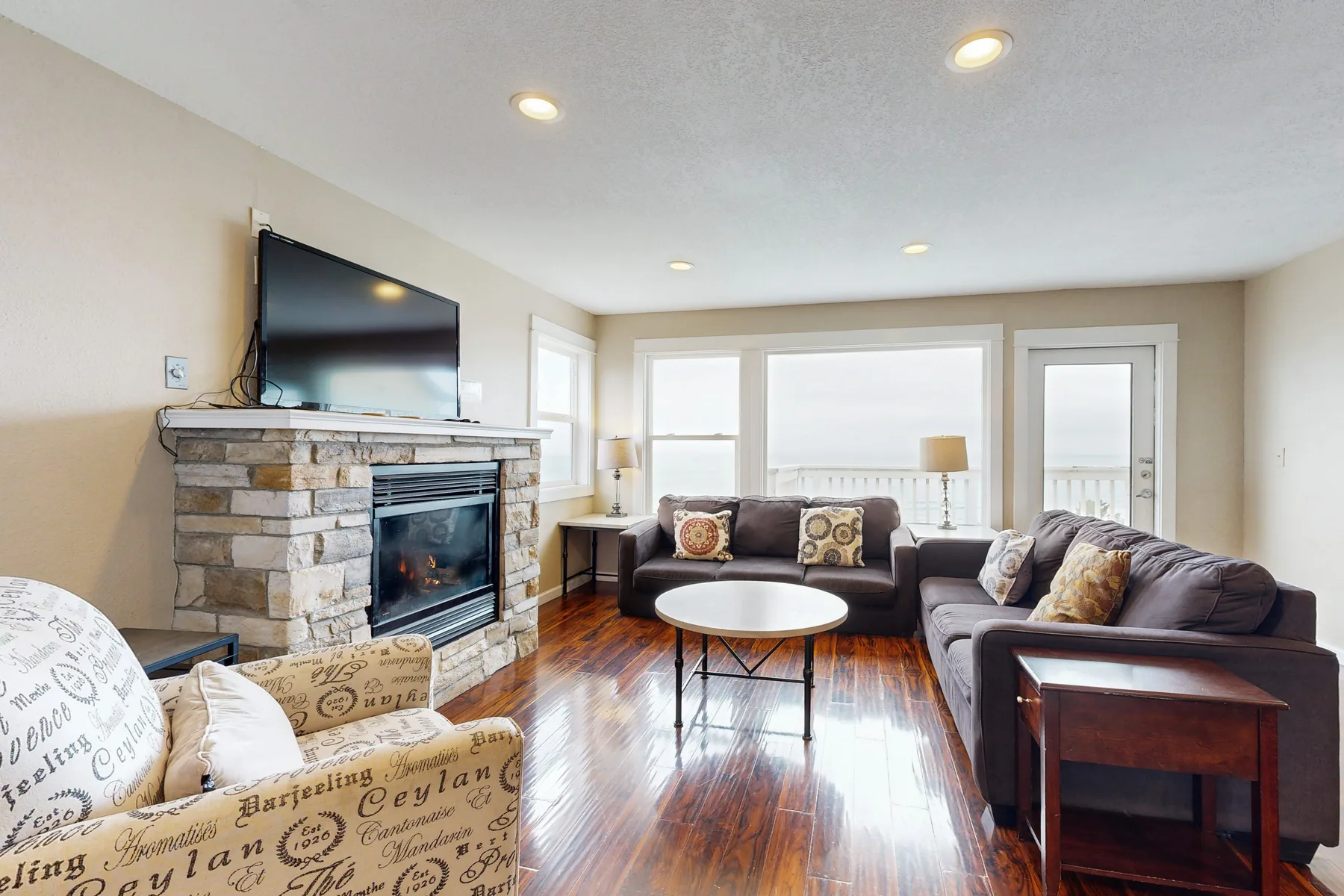A living room with seating arranged around a coffee table beside a stone fireplace.