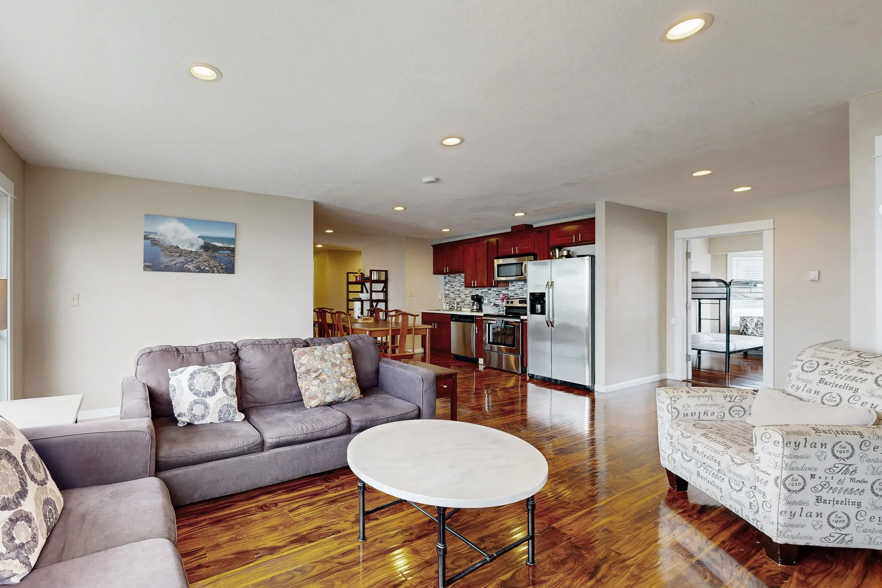 A living room with seating and a round coffee table opens onto a kitchen.