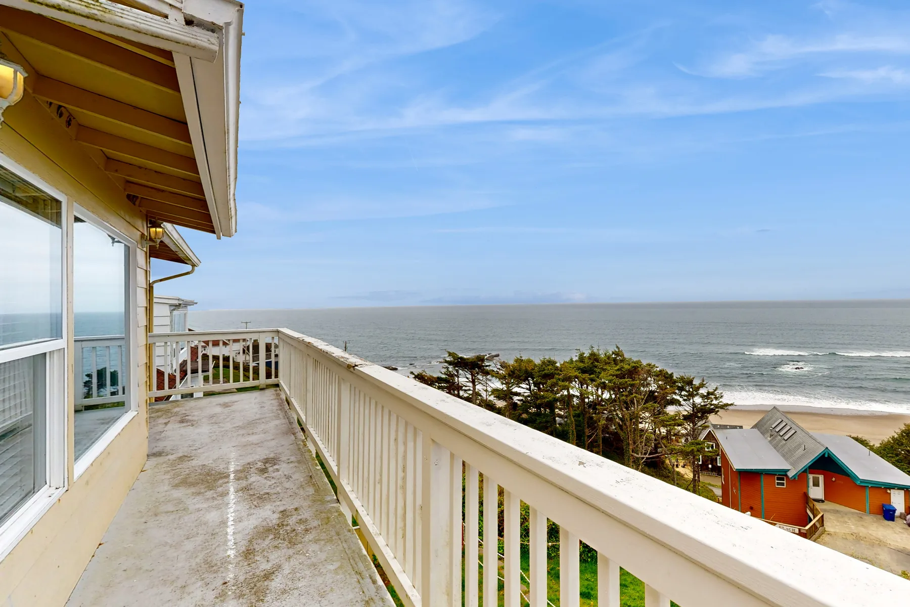 A balcony overlooks the ocean, with trees and houses along the shore.