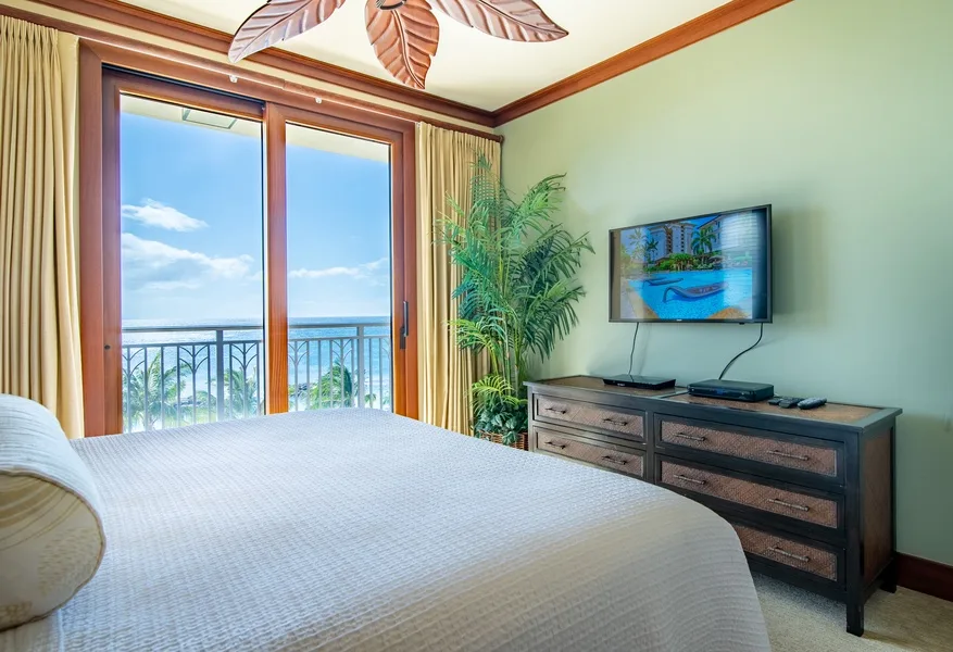 A bedroom with a bed, a television, and glass doors opening onto a balcony.