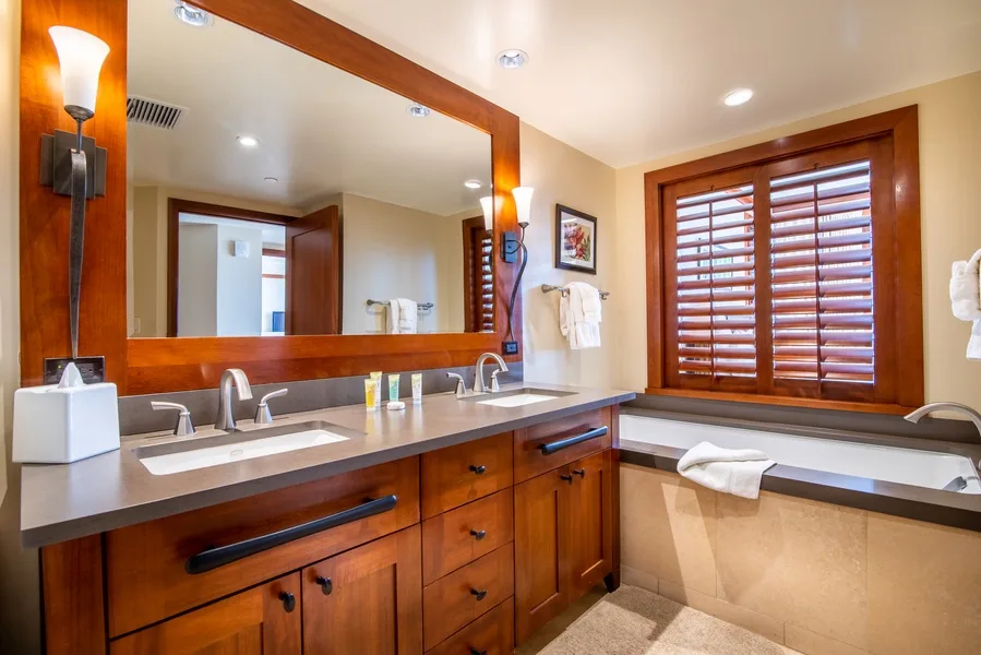A bathroom vanity with a large mirror and a bathtub beside a shuttered window.