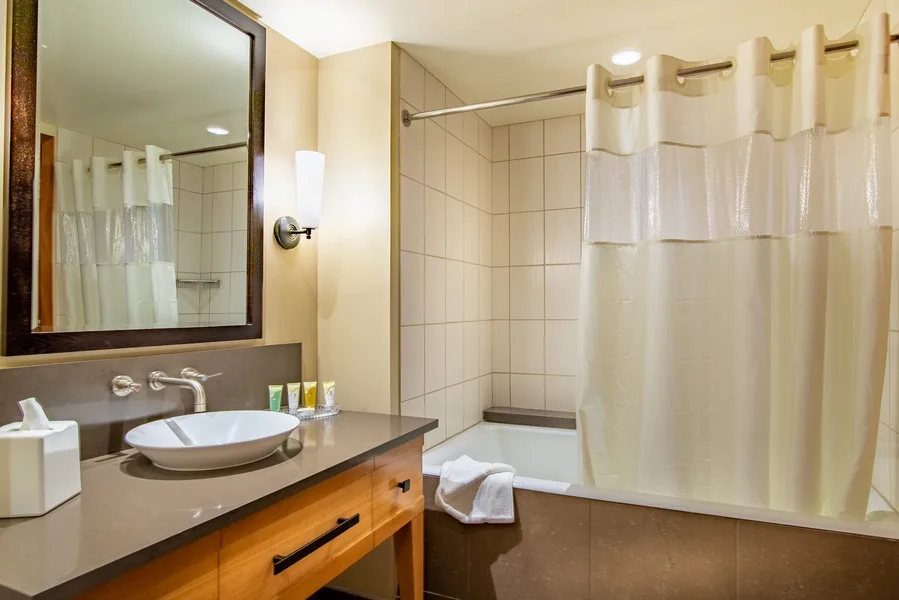 A bathroom with a sink, mirror, and curtained shower.