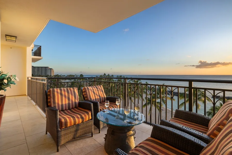A balcony seating area overlooks the ocean beneath a clear evening sky.