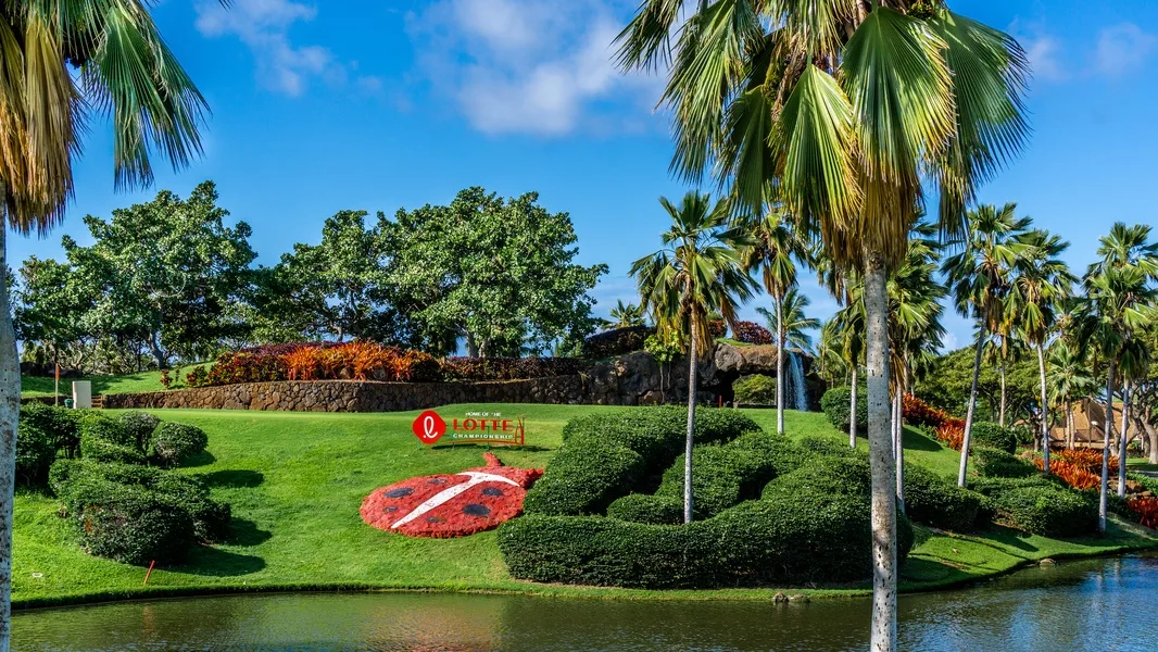 A landscaped hotel garden features palm trees, green lawns, and a flower display.