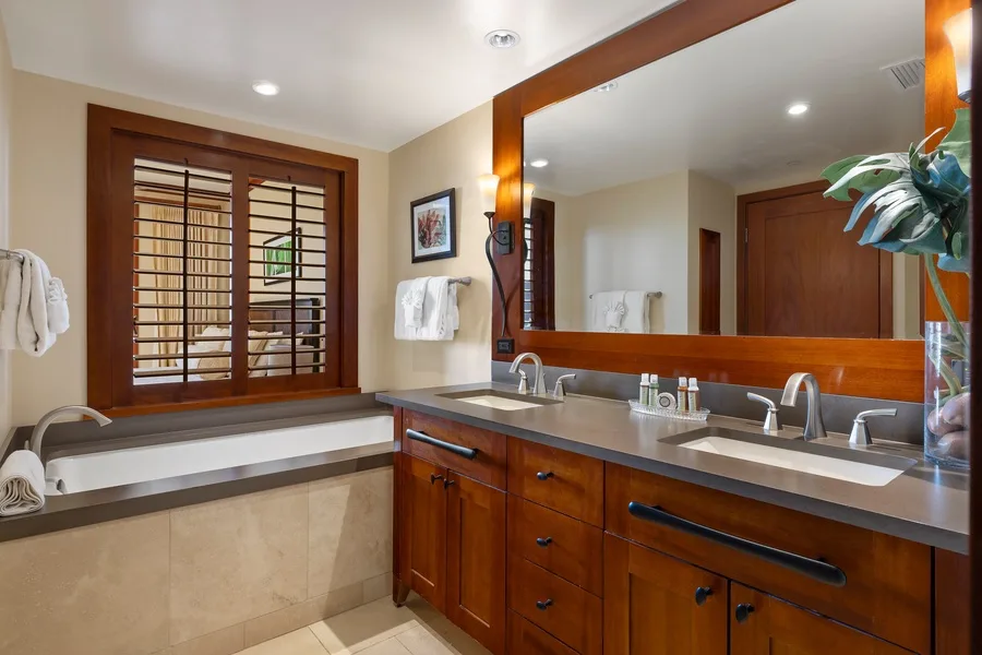 A bathroom vanity with a wide mirror and a soaking tub beside it.