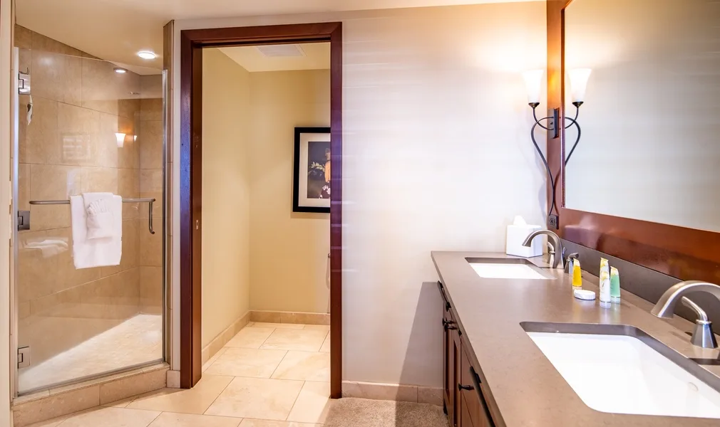 A bathroom with a glass shower and a long vanity with two sinks.