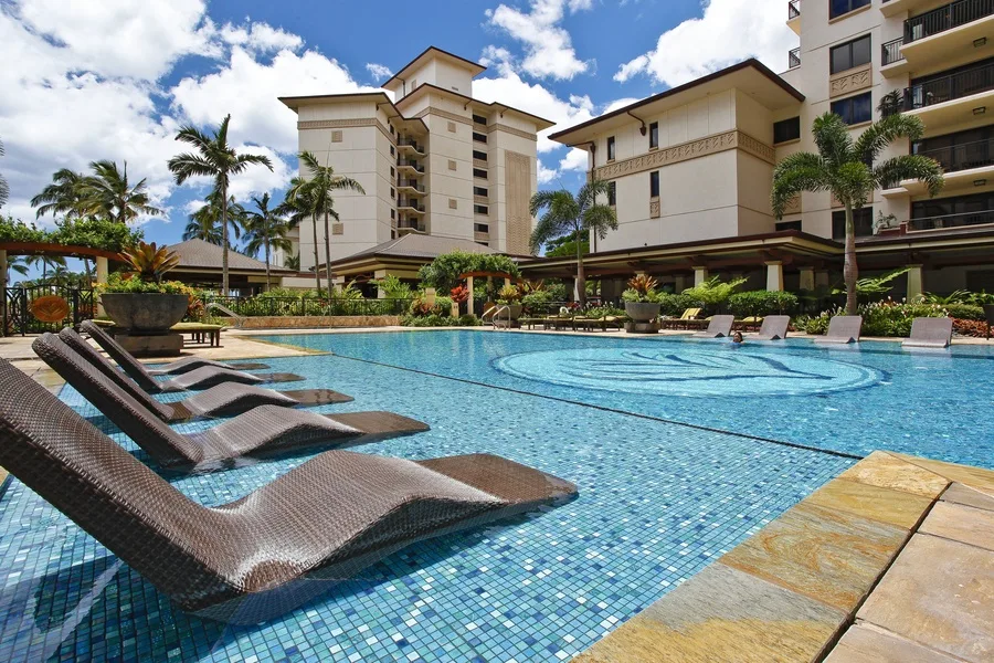 An outdoor swimming pool with submerged lounge chairs and buildings in the background.