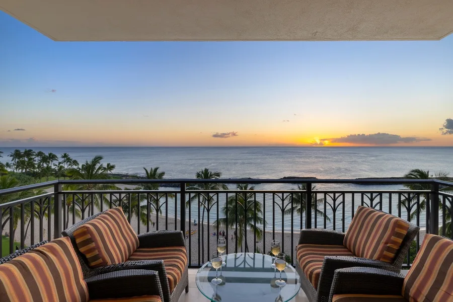 A balcony seating area overlooks the ocean at sunset.