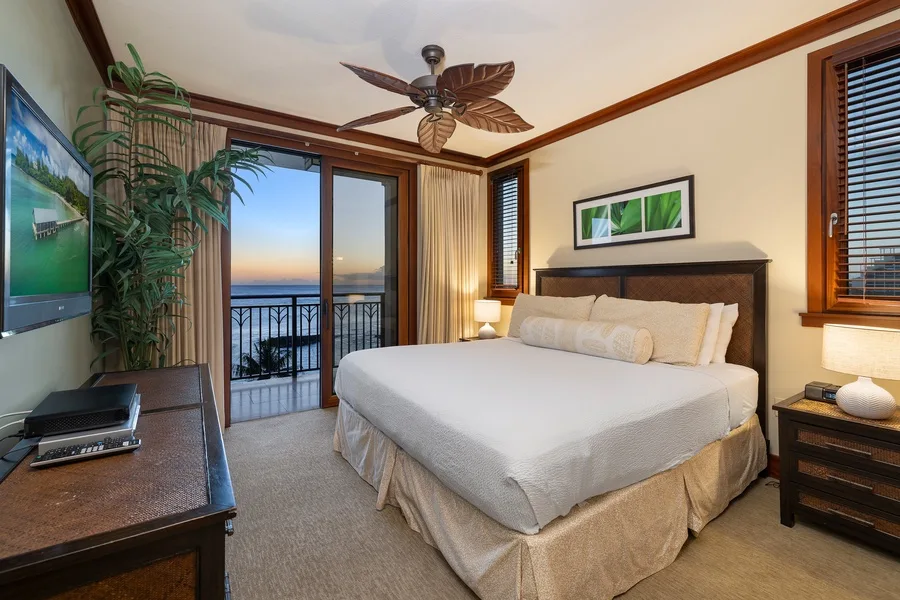 A bedroom with a neatly made bed, windows, and a ceiling fan.