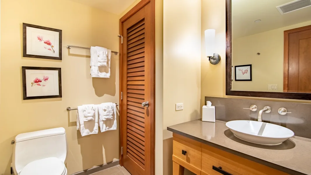 A bathroom with a sink, mirror, toilet, and wooden louvered door.