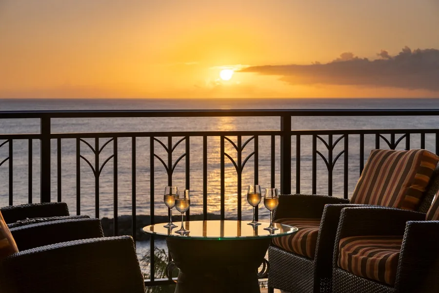 Outdoor seating overlooks the water as the sun sets beyond the railing.