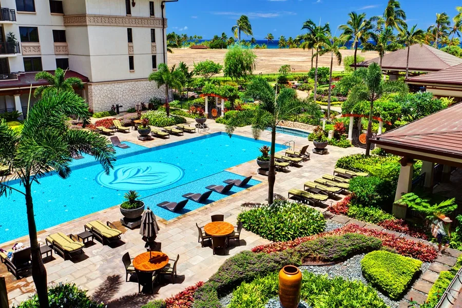 A landscaped pool area with lounge seating, palm trees, and buildings nearby.