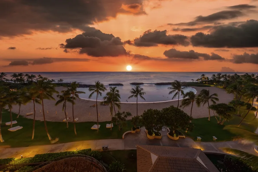 A tropical beachfront landscape at sunset, with palm trees along the shore.