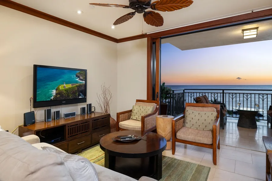 A living room with seating and a television opens onto a balcony overlooking the sea.