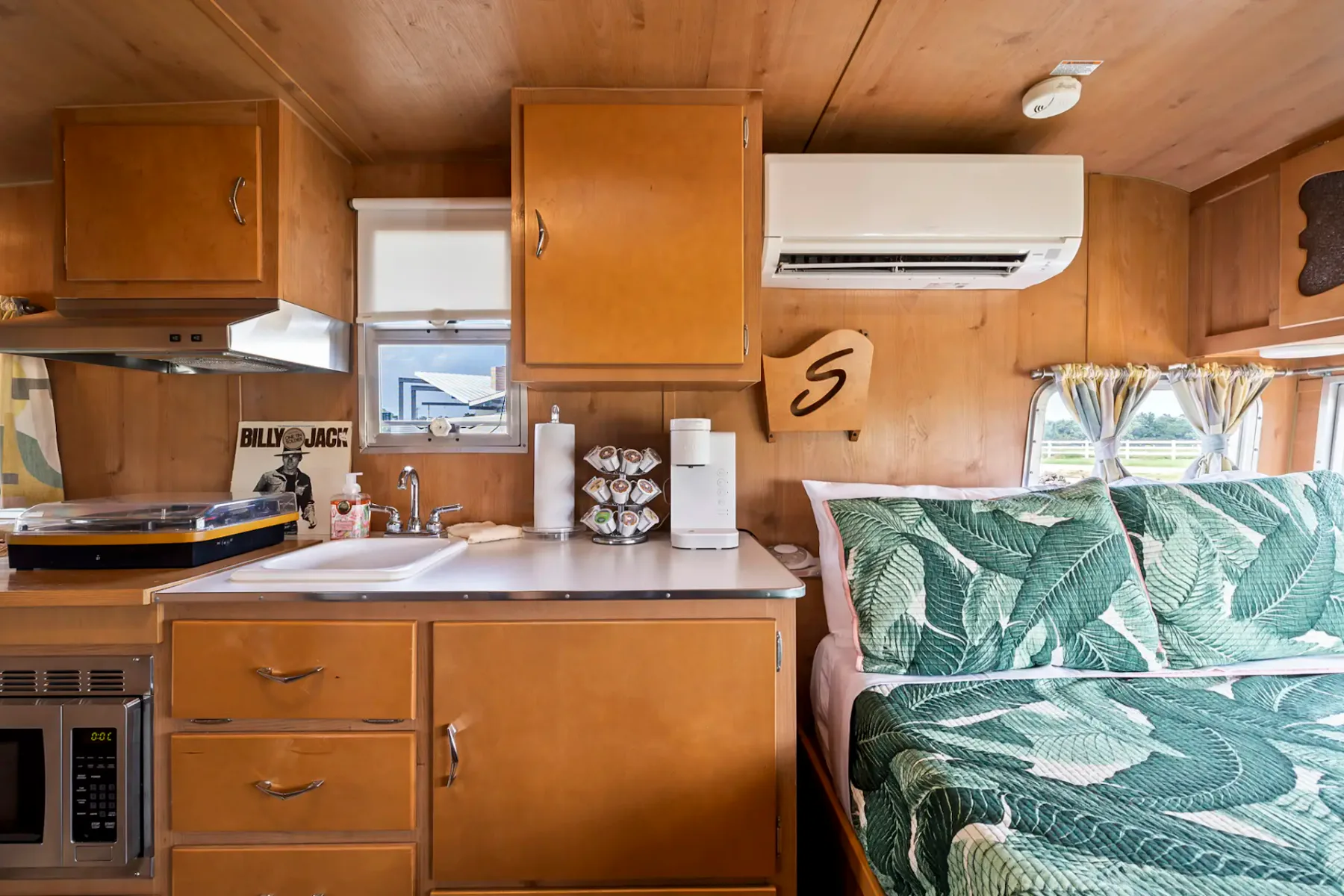 Interior of a cozy camper van with wooden cabinets, checkered floor, and a seating area. Includes a sink, refrigerator, and small TV.