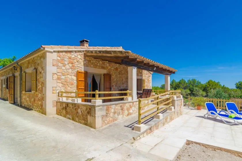 Una casa de piedra con terraza cubierta da a un patio soleado y pavimentado.