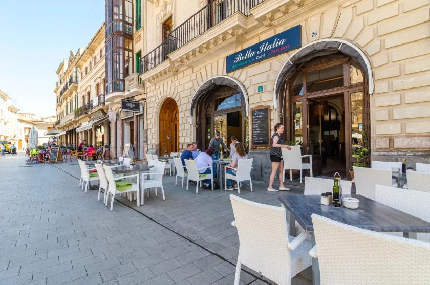 Una terraza de café al aire libre con mesas y asientos junto a una calle peatonal pavimentada.