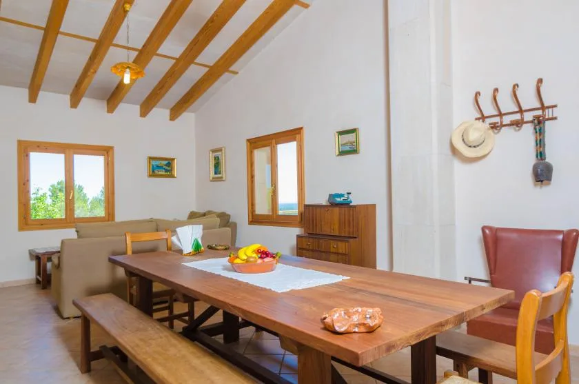 Comedor con una larga mesa de madera y asientos bajo vigas de techo expuestas.