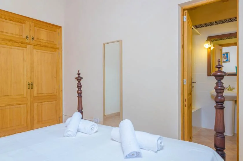 Un dormitorio con una cama, toallas dobladas y un armario de madera junto a una puerta abierta.