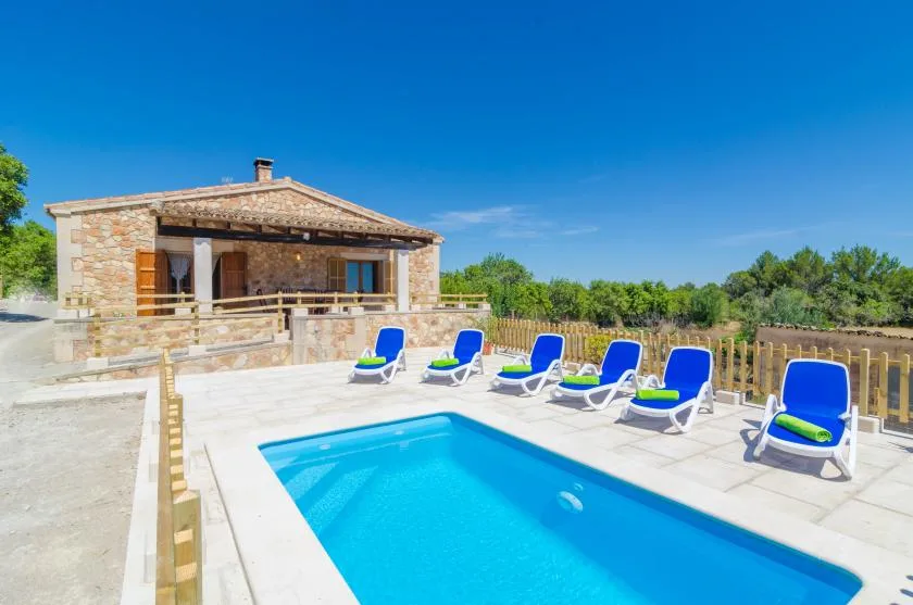 Una piscina está junto a una casa de piedra, con asientos reclinables en la terraza.