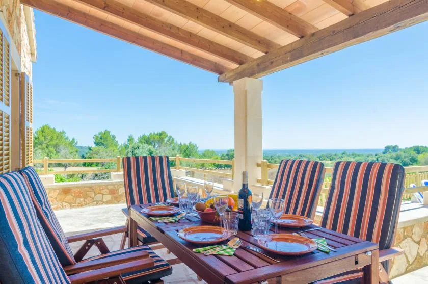 Comedor exterior cubierto con una mesa puesta y asientos a rayas, frente a la vegetación.