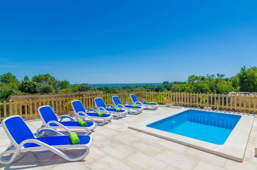 Una piscina al aire libre junto a una terraza pavimentada con asientos azules.