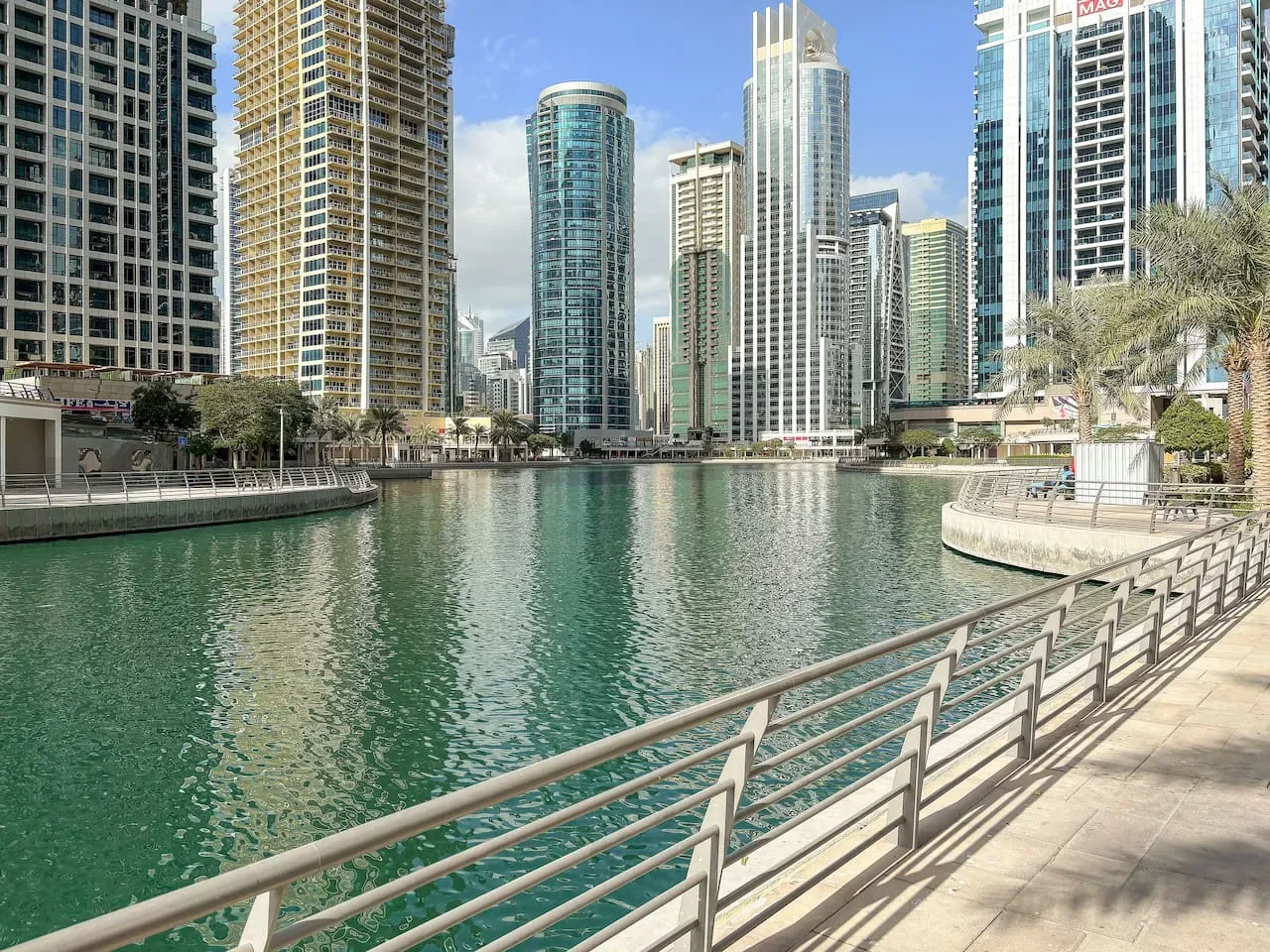 Un paseo junto al agua bordea un canal, con modernos edificios altos al otro lado.