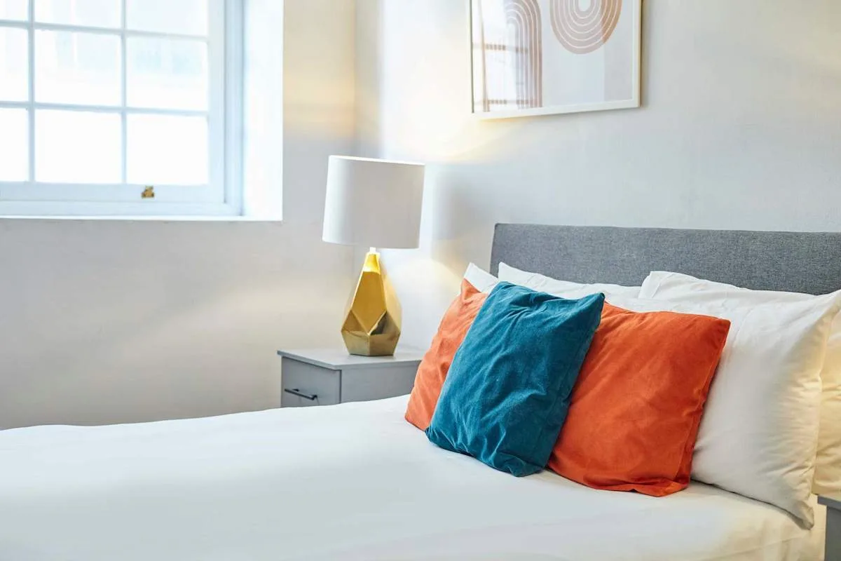 A bright bedroom with a neatly made bed and colorful pillows.