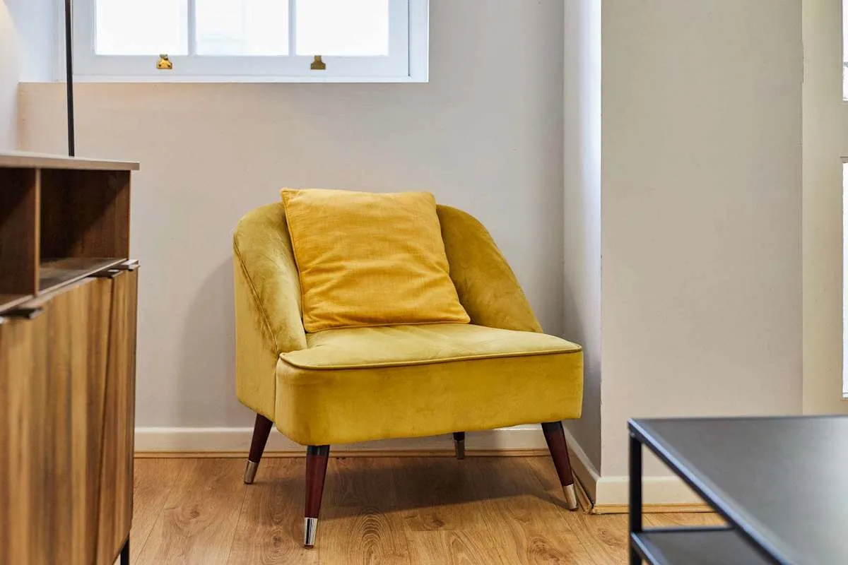 A bright living area with a mustard-yellow armchair beside a wooden cabinet.