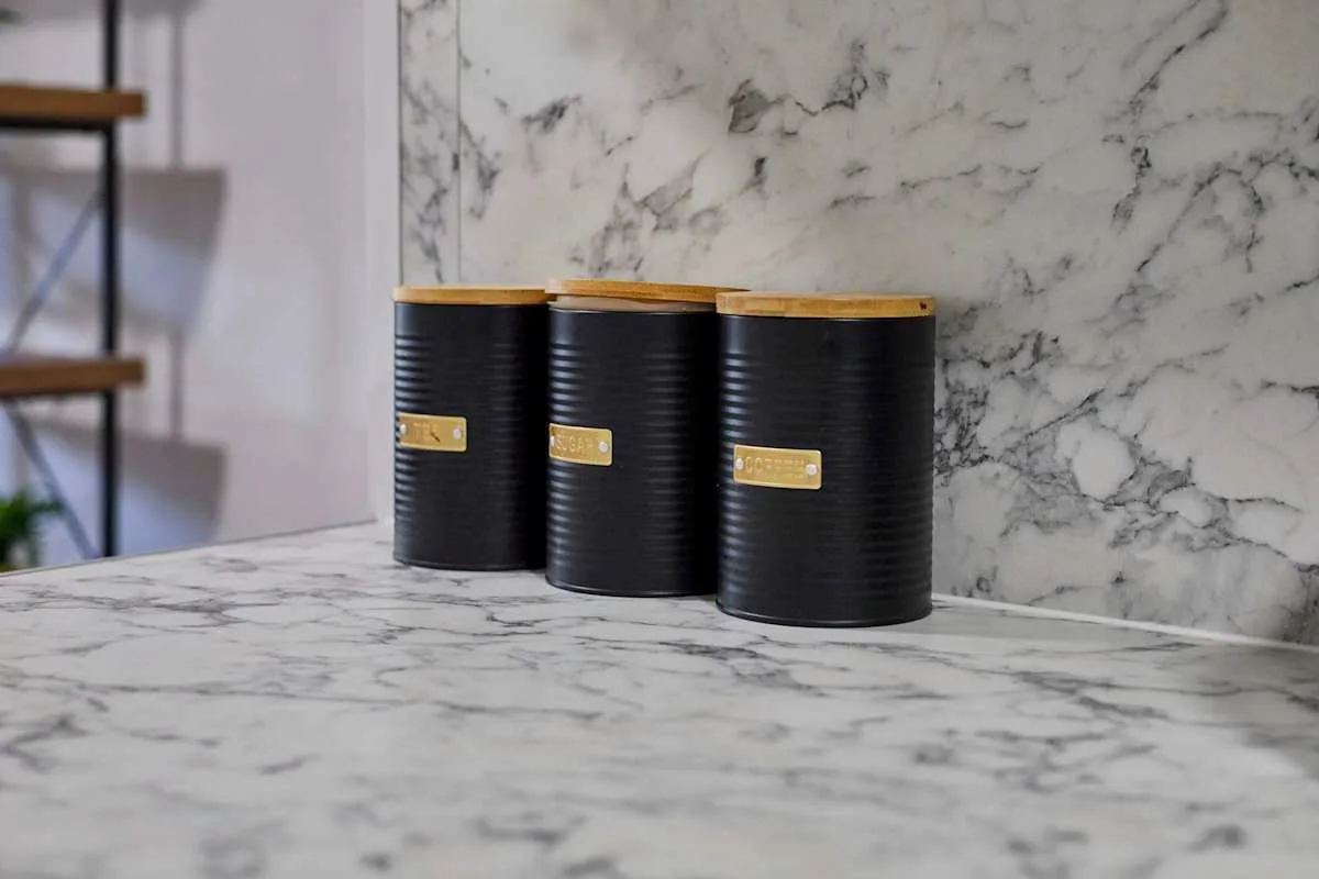 A kitchen counter with three black canisters against a veined backsplash.