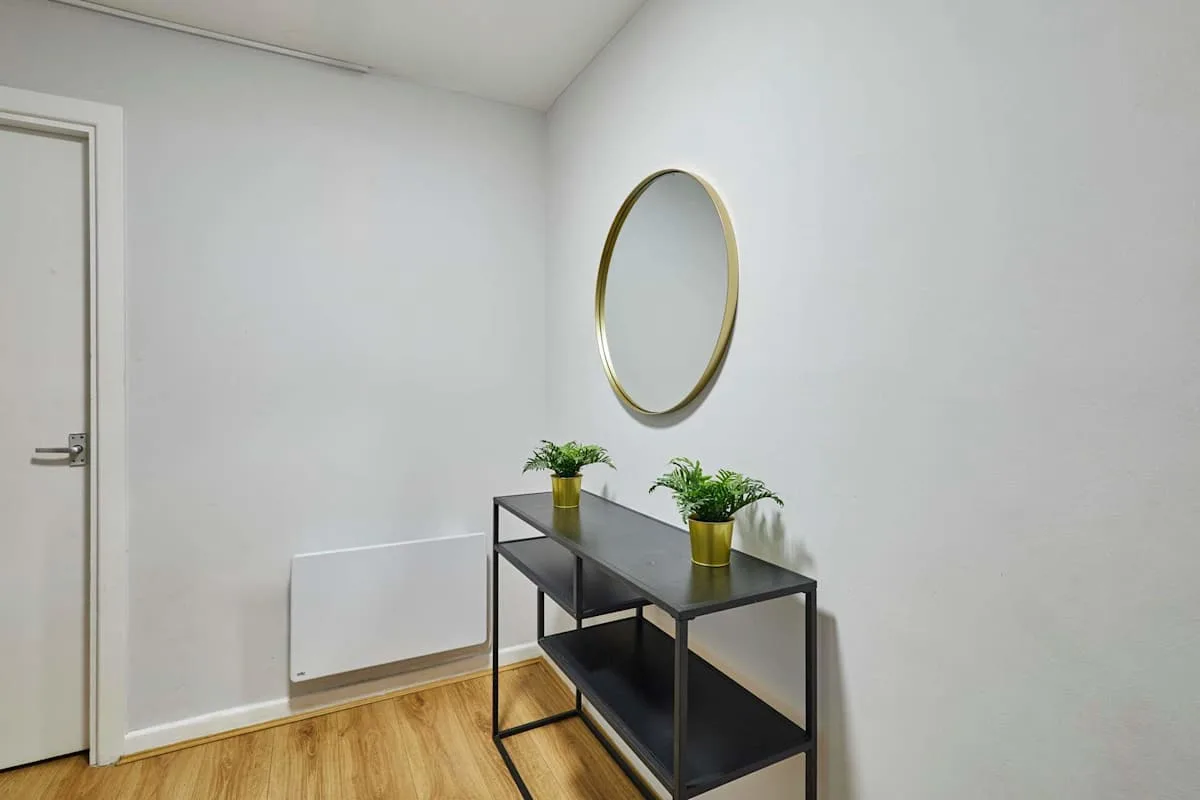 A bright hallway features a black console table with plants beneath an oval mirror.