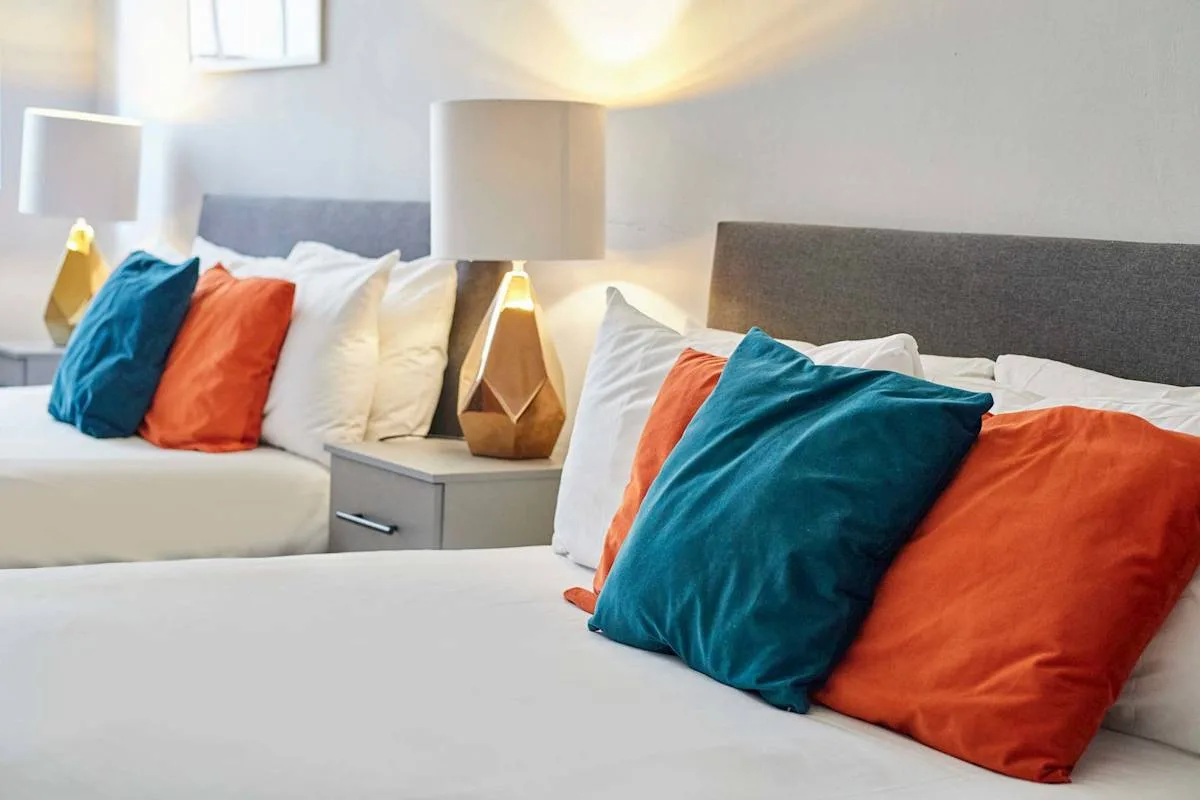 A bedroom with two beds dressed in white and colorful accent pillows.
