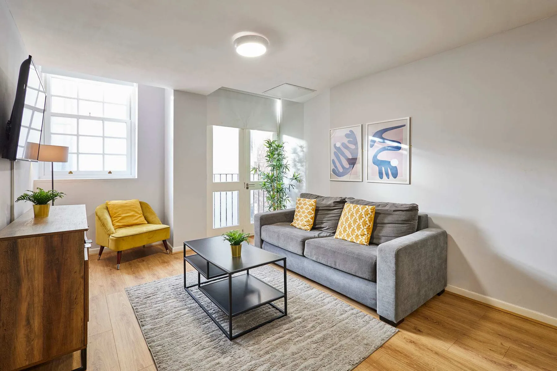 A bright living room with gray seating, a coffee table, and large windows.