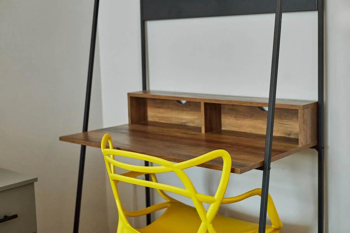 A compact desk with open shelving and a bright yellow chair.