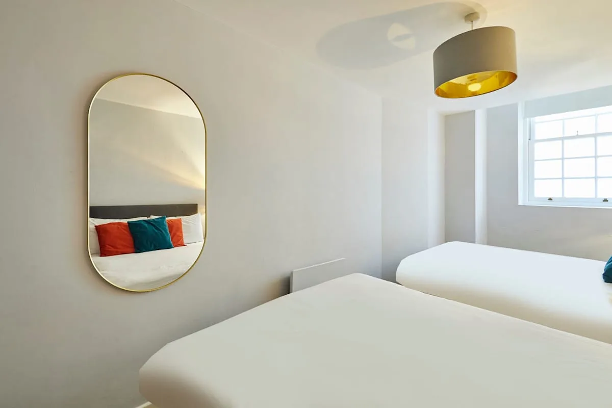 A bright bedroom with white bedding, colorful cushions, and a window.