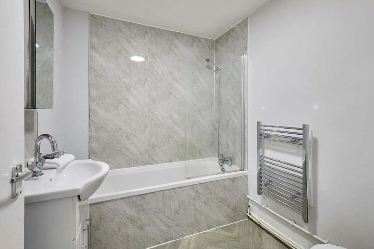 A bathroom with a bathtub, shower, and wall-mounted towel rail.